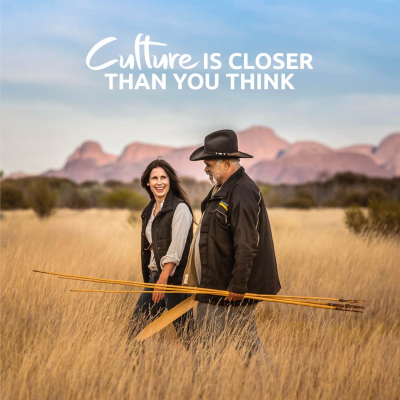 image of woman with Aboriginal guide holding spearks and walking through long grass