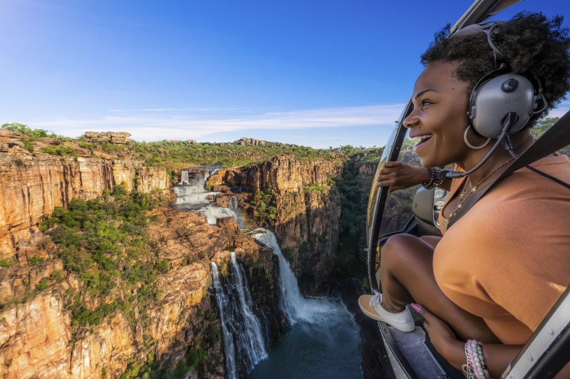 A lady looks out the doors of a helicopter flying over Jim Jim Falls in Kakadu National Park