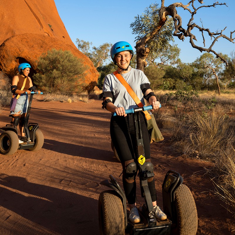 two women riding segways with Uluru in background